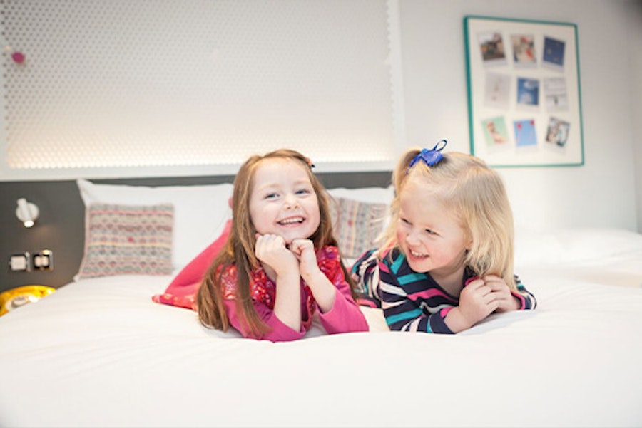 Two little girls laughing on a bed in a hotel room