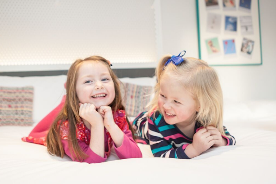 Photo of two smiling young girls lying on a bed in a well-decorated room.