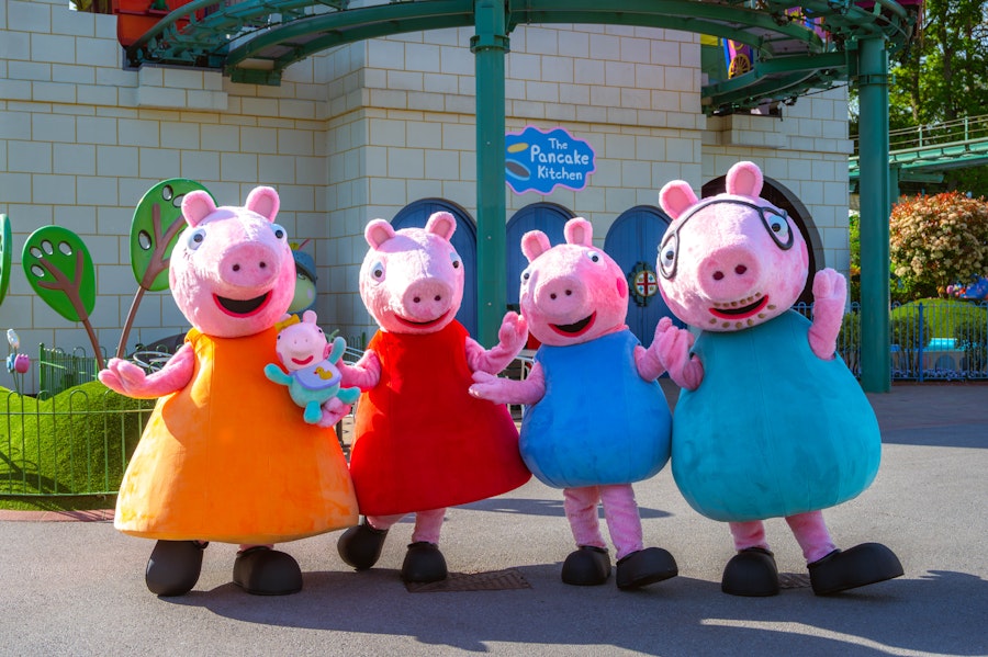 Illustration of two parent pig characters with their two piglet children on a blue cloud with the text 'Peppa Pig World' and a trademark symbol.