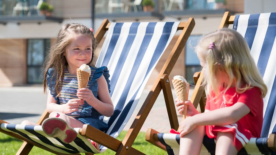 2 little girls sat on deck chairs eating ice creams